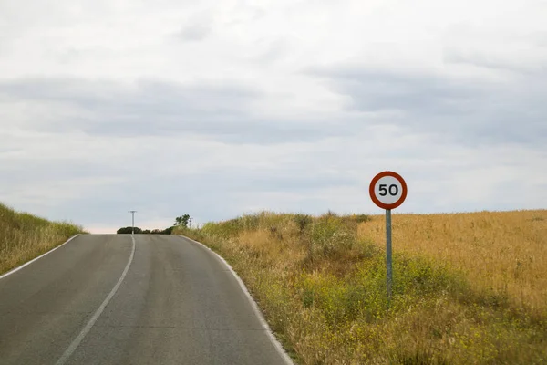 stock image Circular empty road sign limiting the speed of cars to 50 kilometers per hour. Road sign on the side of a country asphalt road in a curve. Gloomy day with rainy clouds on the sky. Rural landscape. 