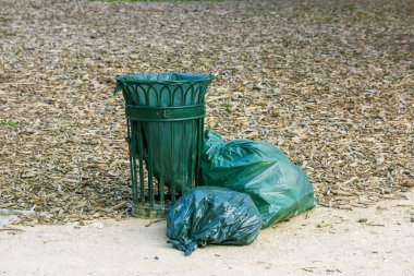 Sokaktaki yeşil metalik çöp tenekesi şehir parkında. Asfaltta her türlü çöple dolu organik ekolojik çöp torbaları. Doğayla ilgili çöp kutusu. Temiz çevre, ekoloji kavramı. 