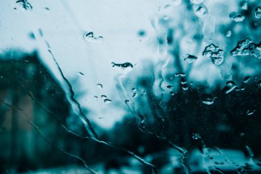 Araba ön camında su akıntıları, soğuk bir sonbahar akşamında eriyen kar. Soyut koyu mavi arkaplan. Kötü hava, yağmur, kasırga, fırtına. Otomobilin, arabanın, evin içinden görüntüle.