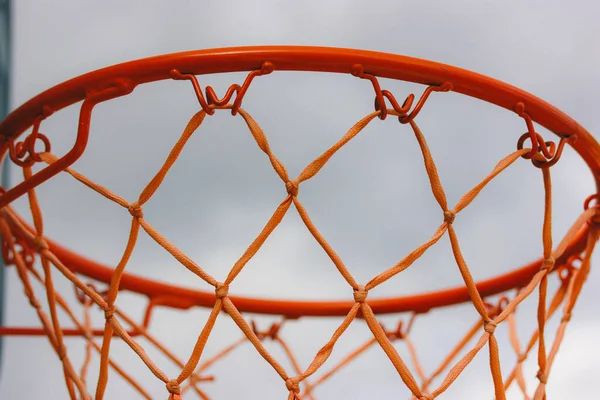 Basketball hoop on backyard against blue sky. Sports recreation and healthy living in nature. Orange red rope net on a street. Equipment on a playground. Training tools on stadium. Play outdoors.
