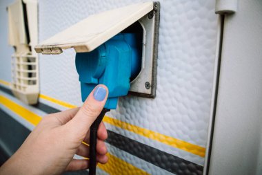 Karavan için endüstriyel elektrik kutusu. Güç kaynağı. Voltaja bağlı karavan şarjı. Kamp aracı kadın eliyle şarj oluyor. Bir kadın arabaya elektrik yüklüyor. Mobil ev elektriği.