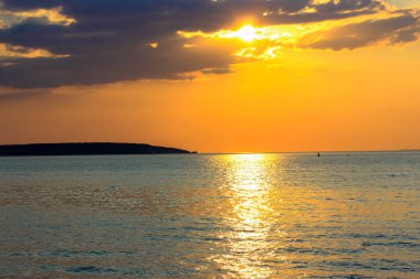 Deniz kıyısında güzel bir gün batımı. Gün batımında görkemli bulutları olan turuncu mavi gökyüzü. Sakin bir su ve güneşli bir şeridin yüzeyi. Tatil için deniz kıyısına seyahat. Doğanın güzelliği, uyum kavramı