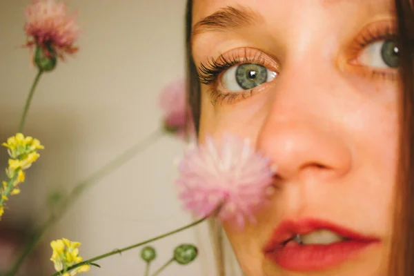 Stock image Beautiful young woman with blue eyes sniffing fresh wildflowers in a vase. Women's portrait close-up. Macro photo of flowers. Blue-eyed white girl selective focus. Summer, springtime nature bloom.