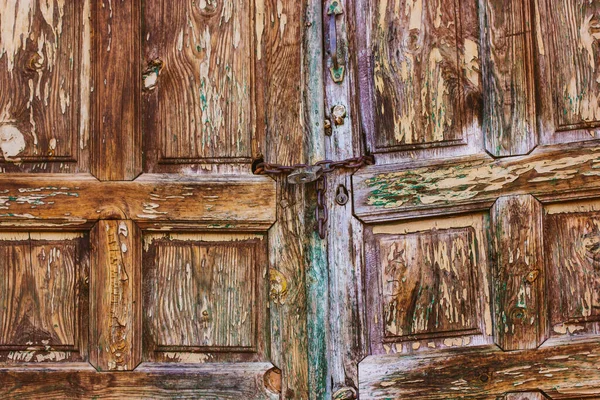 stock image Old wooden dilapidated doors exterior of residential building. Vintage retro wooden brown green yellow door, doorway, entrance. The gates closed on metal chain A shabby wood surface with peeling paint