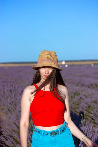 stock image Happy slim stylish woman in straw hat, blue jeans Female portrait on lavender field. Traveling to nature on summer vacation. Travel in spring to Provence, France. Happy girl in red top Happy traveller