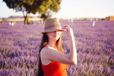 Lavanta çiçekli bir tarlada hasır şapka takan romantik bir esmer kadın yüzünü gizliyor. Bir yaz gününde doğada bir kadın portresi. Avrupa 'da seyahat. Boho tarzı kıyafetler. Provence, Fransa