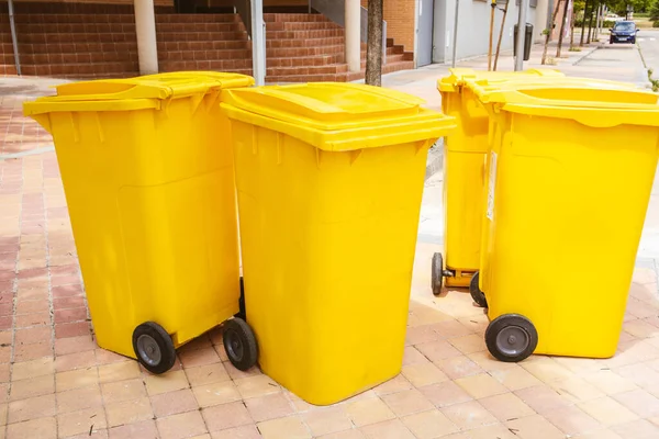 Four yellow plastic trash cans stand on a city street near apartment buildings in a residential neighborhood. Urban Scene. Ecology, cleanliness concept. Gathering rubbish. Wheelie trash bins outdoors.