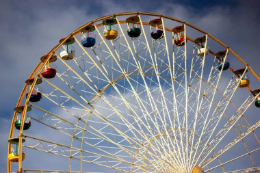 Mavi arka planda şeffaf kabinleri olan beyaz bir dönme dolap. Şehir eğlencesi. Luna park oyunları, çocuklar için eğlence, atlı karınca. Aşağıdan yüksek inşaat manzarası. Kumarbazlar için bir cazibe.. 