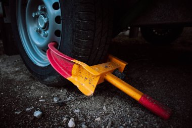 A clamp is used to secure a front wheel of the automobile during transportation, repair. Orange and red wheel blocker. A locker for a car, automobiles. Unpaid parking. Booted vehicle on a city street. clipart