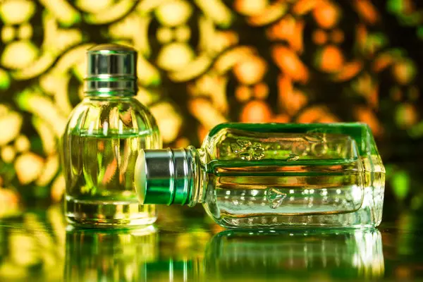 Unbranded perfume bottles on green yellow background. A glass bottle of eau de toilette fragrance water. No brand female cosmetic advertisement. Toiletry for women. Beauty product wallpaper.