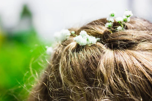 Wedding hairstyle. White flowers in curly hair on a woman's head. Little girl at christening. Bride fashion. Light blond curls on green natural background. First comunion Spain. Floral decor close up