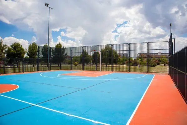 Empty outdoor basketball court in the garden and blue sky. Blue red basketball court for soccer, outside in sunny summer day. A modern playground for sports without people. Playground flooring.