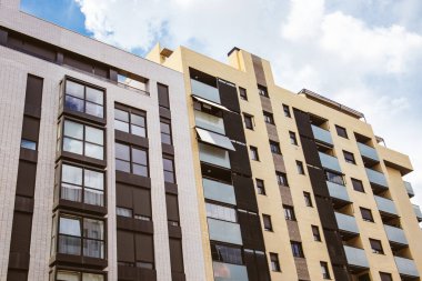 Modern çok katlı binaların bej rengi ve sarı cepheleri, alt kattan manzaralı evler. Ev detayları, mimari dış görünüş düşük açı. İnşaat, emlak yatırımı, konut. 