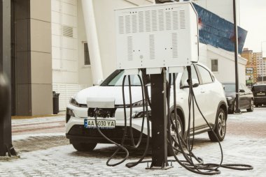 Kyiv, Ukrayna 2 Şubat 2023 Bir elektrik santralinde beyaz bir elektrikli araba şarj edilir. Kışın elektrik dolum istasyonunda ekolojik ulaşım. Şehir caddesinde arabalar için park yeri.