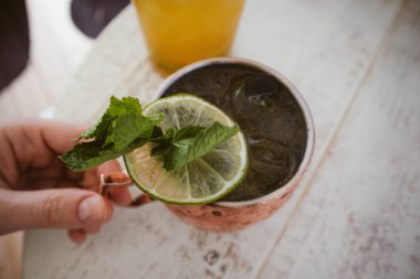 Bir kadın limon, nane yaprağı, tarçın ve zencefilli alkollü kokteyl içiyor. Barda, bir kafede, ahşap bir masada içki servisi yapmak. Soğuk Moskova katır kokteyli Bakır bardak içinde kadın elinde.