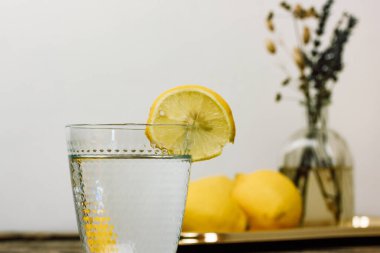 Tahta bir taşra masasında taze limonlardan yapılmış ev yapımı limonata ile hayat. Temiz suyla kesilmiş bir cam ve tarla çiçekleriyle dolu bir vazo ile güzel bir kompozisyon. Limon dilimiyle doldurulmuş su..