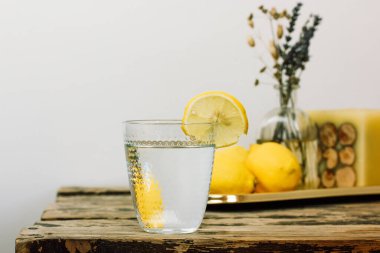 Tahta bir taşra masasında taze limonlardan yapılmış ev yapımı limonata ile hayat. Temiz suyla kesilmiş bir cam ve tarla çiçekleriyle dolu bir vazo ile güzel bir kompozisyon. Limon dilimiyle doldurulmuş su..