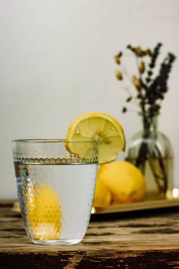 Tahta bir taşra masasında taze limonlardan yapılmış ev yapımı limonata ile hayat. Temiz suyla kesilmiş bir cam ve tarla çiçekleriyle dolu bir vazo ile güzel bir kompozisyon. Limon dilimiyle doldurulmuş su..