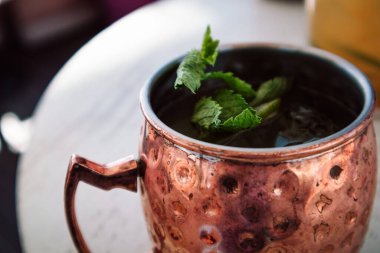 Limonlu, nane yapraklı, tarçınlı, zencefilli alkollü kokteyl. Kafede, bir barda, ahşap bir masada içki servisi yapmak. Soğuk soğuk Moskova katır kokteyli bronz altın bakır bardakta. Detayları kapat.