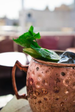 Limonlu, nane yapraklı, tarçınlı, zencefilli alkollü kokteyl. Kafede, bir barda, ahşap bir masada içki servisi yapmak. Soğuk soğuk Moskova katır kokteyli bronz altın bakır bardakta. Detayları kapat.