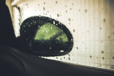 Camında yağmur damlaları olan yeşil bir araba penceresi. Araba temizleme servisinde içeriden yıkanmış. Sabunla araba yıka. Yeşil filtreli fotoğraf. Dikiz aynası. 