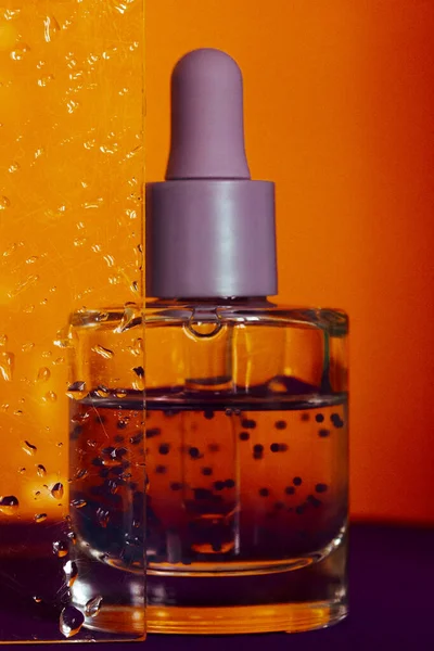 玻璃瓶中的透明质酸 在橙色背景上有一个吸管 与湿玻璃杯抗衡 洗澡间里的面部血清或角质油 补水血清为老化的皮肤提供活性保湿 — 图库照片