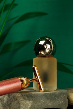 Zümrüt zümrüt zemininde doğal bitkilerle yüz masajı yapan yüksek frekanslı gençleştirici T-Vibe. Yüz ve boyun kaldıran masaj aletleri ve bir şişe yağ, taş podyumda vücut bakımı için gerekli su. 