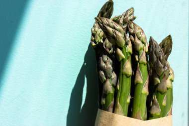 Bir demet taze yeşil çiğ kuşkonmaz lahanası kahverengi bir kravat kağıdına sarılı, açık mavi arka planda zıt gölgelerle birlikte eko poşeti. Faydalı doğal yiyecekler. Organik sebzeler. Sağlıklı beslenme