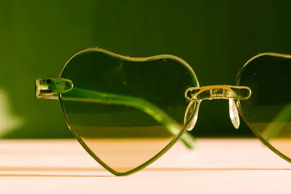 Sunglasses with green glasses in the shape of hearts. Fashion accessories for summer vacation. Female beauty accessory, glamour object. Summertime fun, travel concept. Valentine\'s Day . Fall in love.