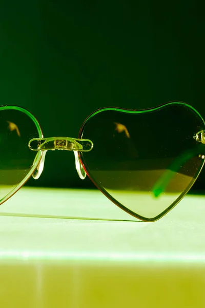 Sunglasses with green glasses in the shape of hearts. Fashion accessories for summer vacation. Female beauty accessory, glamour object. Summertime fun, travel concept. Valentine's Day . Fall in love.