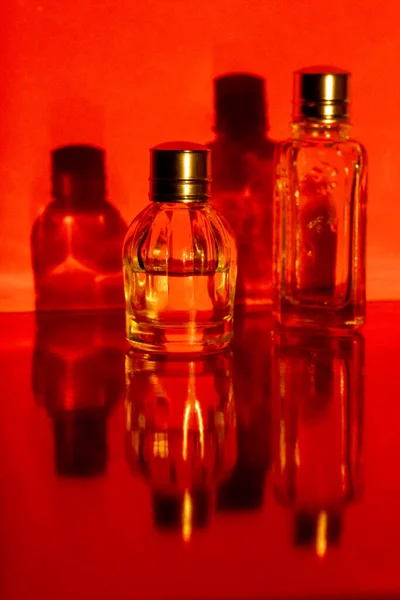 Glass miniature bottles with perfume, essential oils with reflections, shadows. Cosmetic products. Facial and body skin care, beauty shop concept. Women\'s grooming products on red vertical background.