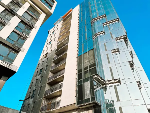 Fragment of modern tall building with glass facade against blue sky. High growing buildings low angle view. Modern multi-story standstill in residential neighborhood. Condominium, apartments for sale.