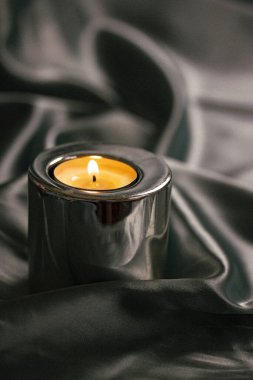 Gümüş ipek masa örtüsüyle kaplı bir masada yanan bir mum. Modern iç mekanlar için lüks bir tarz. Huzur, rahatlama, meditasyon, kendini tanıma konsepti.