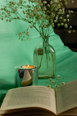 Madrid, İspanya 1 Mayıs 2023 Açık bir ciltli karton kitap yeşil bir masada yatıyor. Küçük narin beyaz çiçekli vazo, bahar için ev dekorasyonu. Sakinleşmek, okumak, çalışmak. İçerde çalışma alanı.