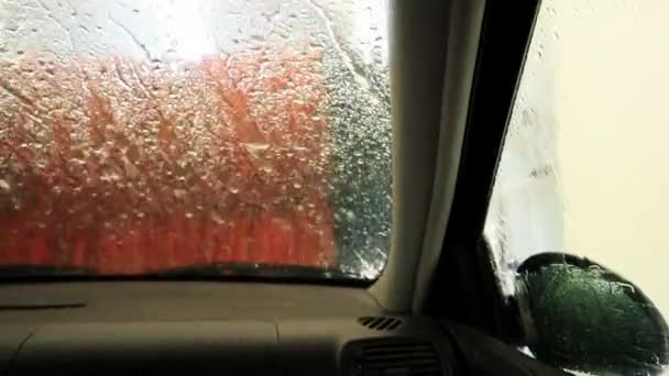 用自动洗车的方式洗车 洗车过程中从车内观察 水滴在潮湿的窗户上 腋下喷出挡风玻璃 一股水柱打在窗户上 — 图库视频影像