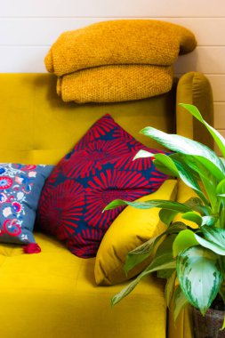 Ev modern iç tasarım ayrıntıları. Hardal sarısı kanepe ve sıcak yün ekoseli dikey fotoğraf, yumuşak dekoratif parlak yastıklar ve kapalı alanda saksı yeşil çiçek. Oturma odası rahat dekor..