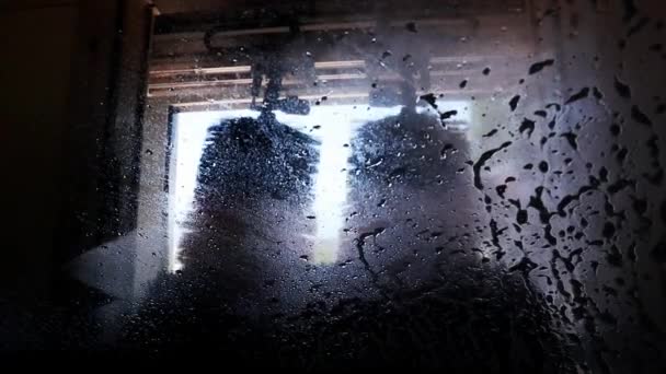 用自动洗车的方式洗车 洗车过程中从车内观察 水滴在潮湿的窗户上 腋下喷出挡风玻璃 一股水柱打在窗户上 — 图库视频影像