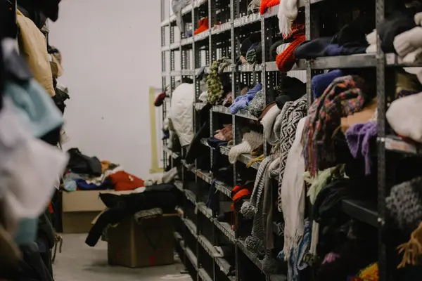 Humanitarian aid station, interior of industrial warehouse with used clothes for poor, refugees, vulnerable people. Shelves, rows of clothes second hand. Stock clothing section collection disordered.