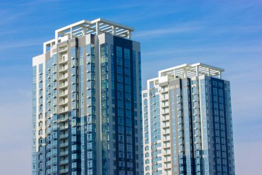 Mavi gökyüzü arka planında iki modern apartman binası. Hazır şantiyeye yatırım. Ofis, kiralık iş yeri. Büyük şehir finans merkezinde bir gökdelen. Emlak.