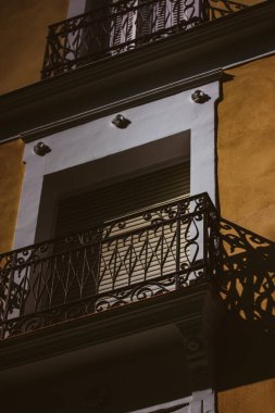 Güneşli günlerde zıt gölgelerle kaplı eski bir ev ve balkon. Sarı bir apartmanın ön cephesi. Tarihi köy, kasaba, şehir. Mimari detaylar. Barok bir sarayın balkonunda..