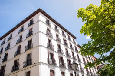 Madrid, İspanya. 9 Mayıs 2022. Klasik mimari tarzında güzel, eski, iyi korunmuş, beyaz bir bina. Mavi gökyüzü ve yeşil yaprakların arka planına karşı beş katlı bir ev. Şehir manzarası.