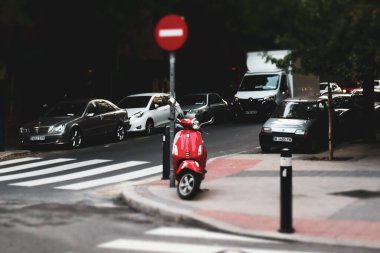 Madrid, İspanya. 19 Kasım 2023 Red Piaggio Vespa scooter 'ı şehir sokağına park etti. Çevre dostu eski model nakliye aracı. Avrupa şehir sokağı. Beyaz yaya geçidi, zebra. Şehir manzarası. Seyahat fotoğrafı.