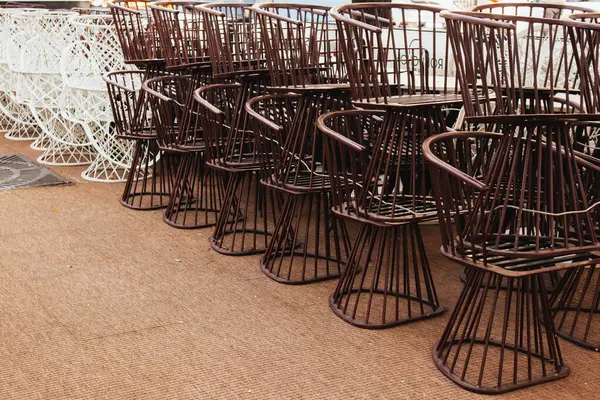 Many metal or iron white and brown chairs stacked outside on cafe, restaurant, bistro terrace. Empty restaurante outdoors. Closed coffee shop. Urban furniture outside. Huge stuck of chairs outdoors.