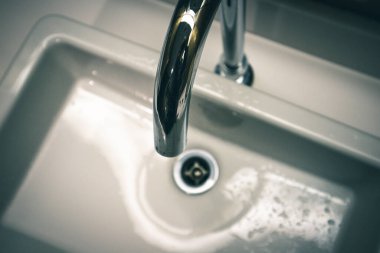 Banyoda paslanmaz su musluğu. Metal musluk ve leğen, borular ve beyaz kare lavabo modern banyo manzarasında. Musluk ve havza ayrıntıları, borular ve kanalizasyon. Ev tuvaletindeki musluk.. 