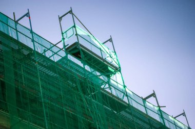 Çok katlı bina yeniden inşa ediliyor. Önü yeşil koruyucu inşaat örgüsüyle kaplı. Büyük şehirlerdeki konut binalarının, evlerin, gökdelenlerin yenilenmesi. Bitmemiş proje