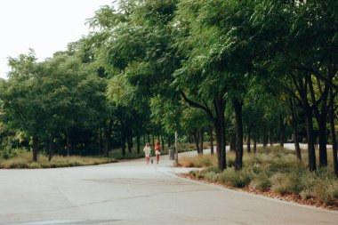 Madrid, İspanya 7 Temmuz 2023. 7 Temmuz 2023. Açık hava eğlencesi için yeşil park alanı. Gündüz vakti sokakta yürüyen insanlar. Modern yaşam tarzı. Yaprak döken ağaçlarla dolu güzel bir park alanı. Peyzaj.