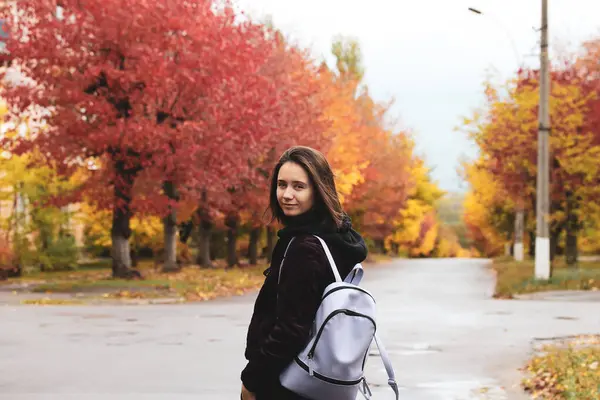 ストリートのバックパックの女の子 秋の季節には赤 黄色の木が植えられています 若い女性は 秋の日に屋外で肖像画を描いている 11月には自然を歩いている人たち 休日のライフスタイルに関する十代の若者 ストック写真