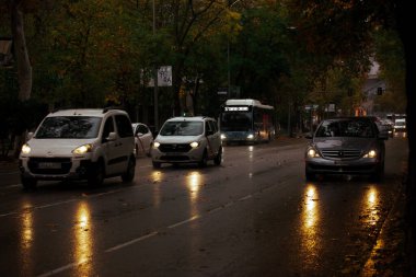 Madrid, Spain November 30, 2023 City street with traffic in the evening. Automobiles with high beam lights on. A rainy day in a town. Wet asphalt road in a twilight. Weather forecast for rainy season. clipart