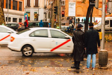 Madrid, İspanya 30 Kasım 2023 Yağmurlu sonbahar gününde şehir caddesinde araba. Trafik ışığı kırmızıyken yaya geçidinde duran yayalar. Beyaz taksi hızlı gidiyor. Şehir halkı yaşam tarzı