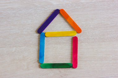 Sembolik oyuncak ev ahşap renkli oyun çubuklarından yapılmış. Memleket gayrimenkul, ev alma ve kiralama konsepti. Parlak renkli ev şekli. Tahta masadaki buz çubuklarından yapılmış ev.